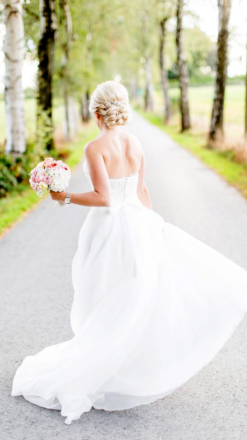 Eine Frau steht mit Brautkleid in einer Allee 