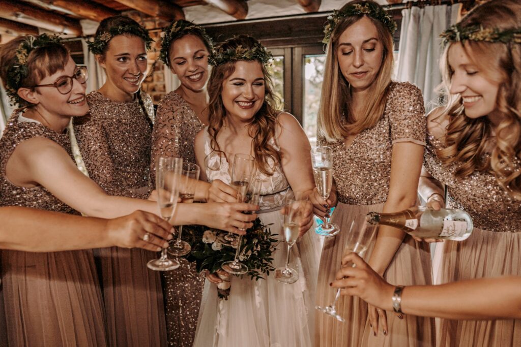Braut und Brautjungfern mit Blumenkränzen stoßen mit Sekt an