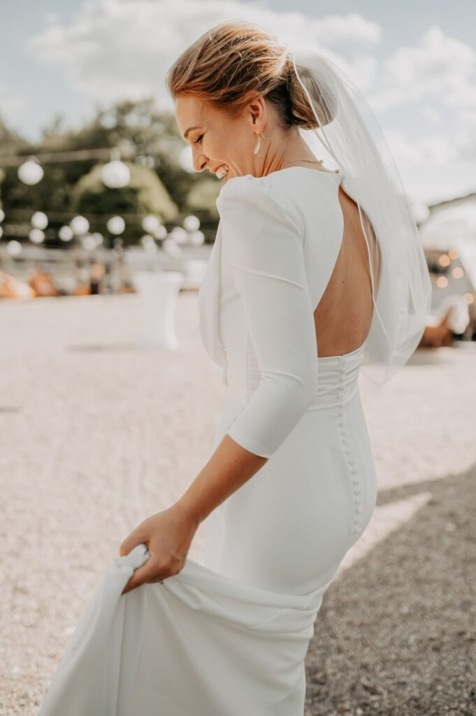 Lachende Braut mit Dutt und Schleier im schlichten Kleid mit Rückenausschnitt