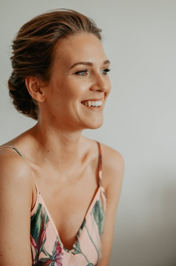 Lachende Braut mit leichtem Make-up und locker hochgesteckten Haaren beim Getting Ready