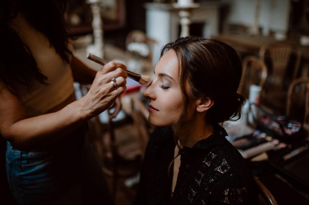 Natalie Aust trägt Lidschatten mit dem Pinsel auf, Braut mit dunklem Haarknoten und schwarzer Spitzenbluse