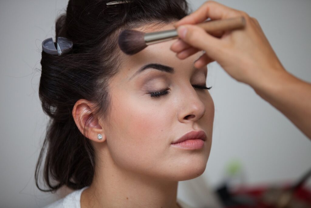 Braut mit geschlossenen Augen beim Pudern, dezentes Augen-Make-up, dunkle Haare mit Clips vorbereitet