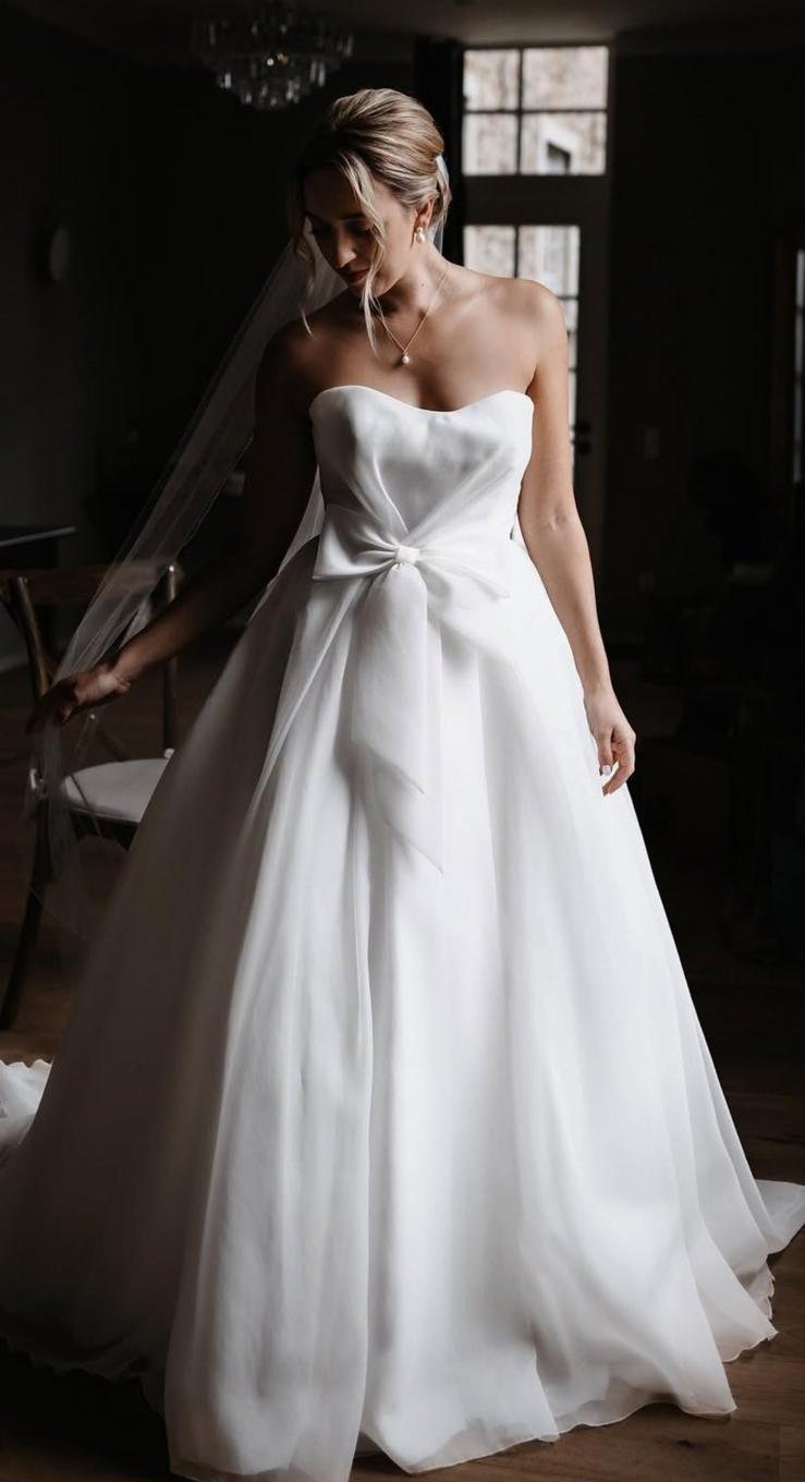Braut mit hochgestecktem Sleek Bun und Schleier im trägerlosen Kleid mit Schleife