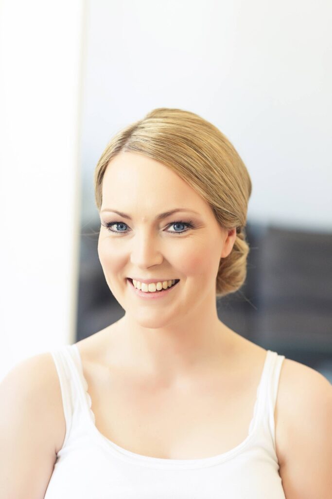 Lächelnde Braut mit tiefem, glattem Knoten und natürlichem Make-up, das die blauen Augen betont