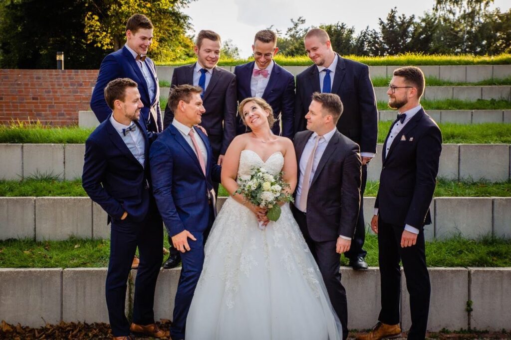 Braut mit Brautstrauß inmitten der Trauzeugen und Freunde in blauen Anzügen
