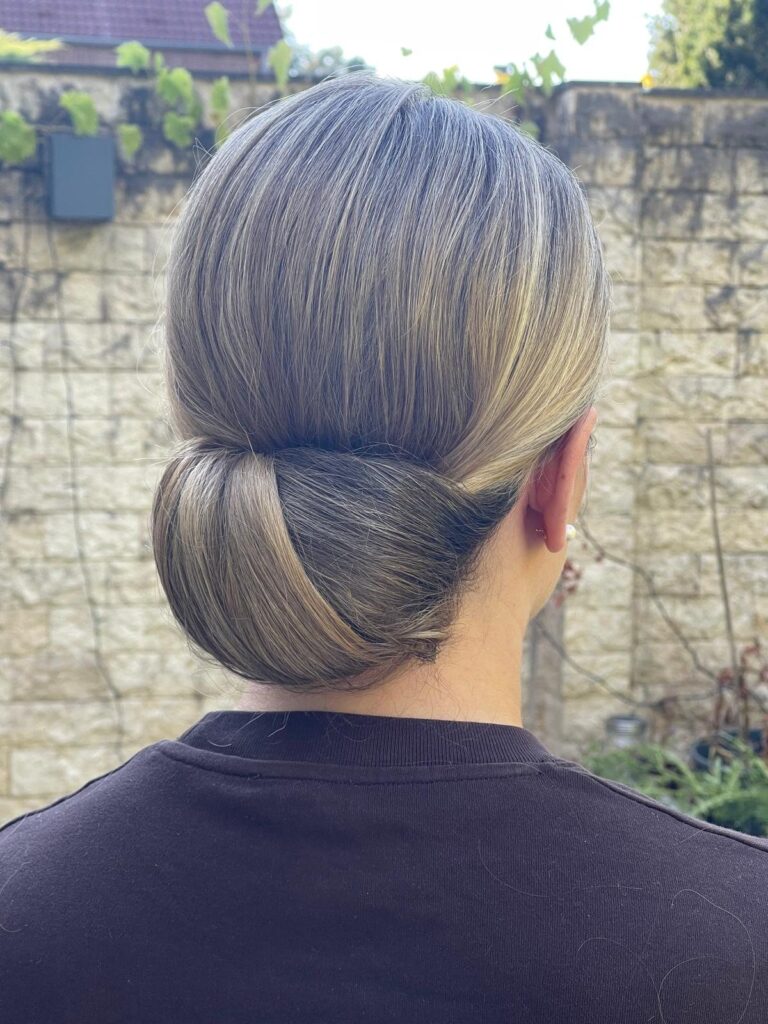 Clean-Chic-Brautfrisur von hinten: glatter, eingerollter Chignon im Nacken