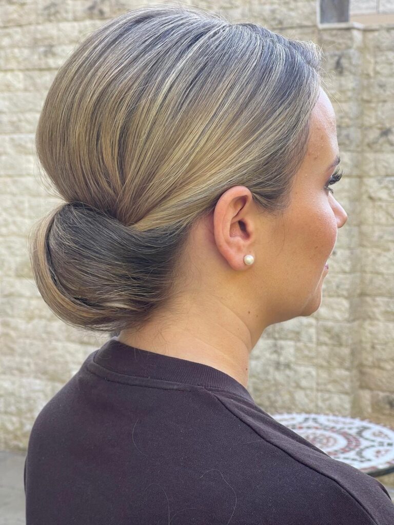 Glatter, tief sitzender Chignon in Blond von der Seite, sauber gesteckte Brautfrisur mit Perlenohrring