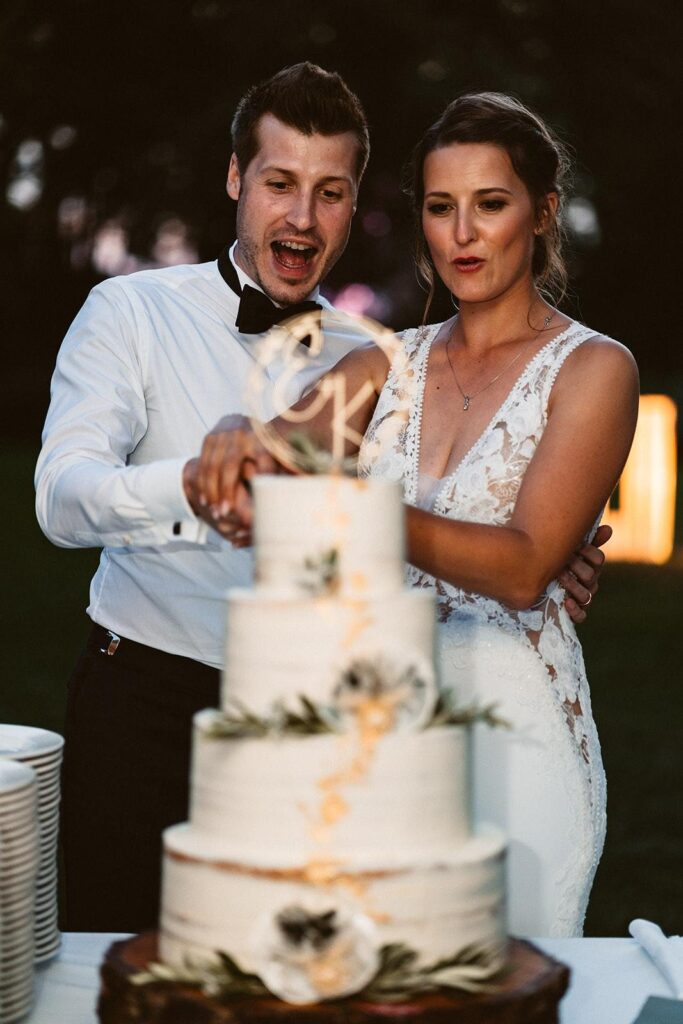 Brautpaar schneidet abends die Hochzeitstorte an, Braut mit Abend-Make-up und Spitzenkleid