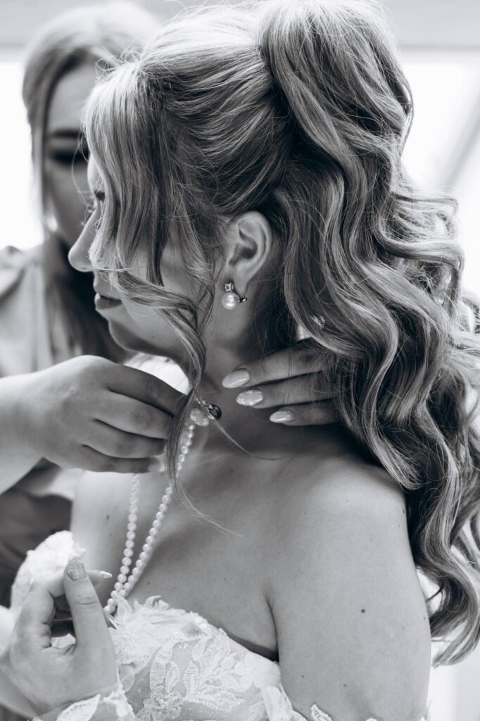 Beim Getting Ready wird der Braut mit halboffener Lockenfrisur die Kette angelegt