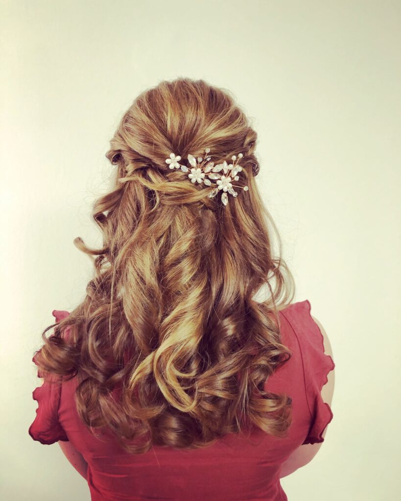 Halboffene Lockenfrisur mit Blüten-Haarschmuck von hinten, getragen zu einem roten Kleid