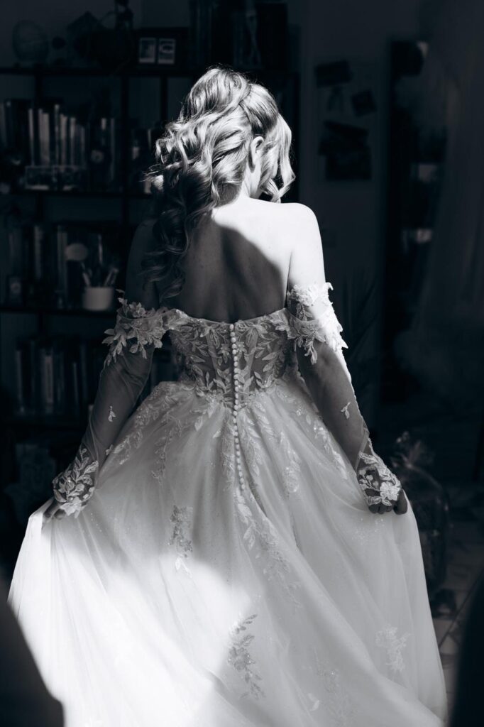 Braut mit halboffener Lockenfrisur von hinten im Spitzenkleid mit Knopfleiste