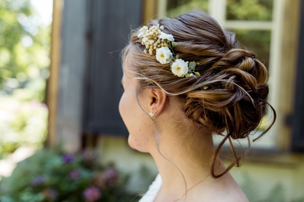 Lockere Hochsteckfrisur mit weißen Blüten und Beeren im Haar, im Profil vor einem Fensterladen