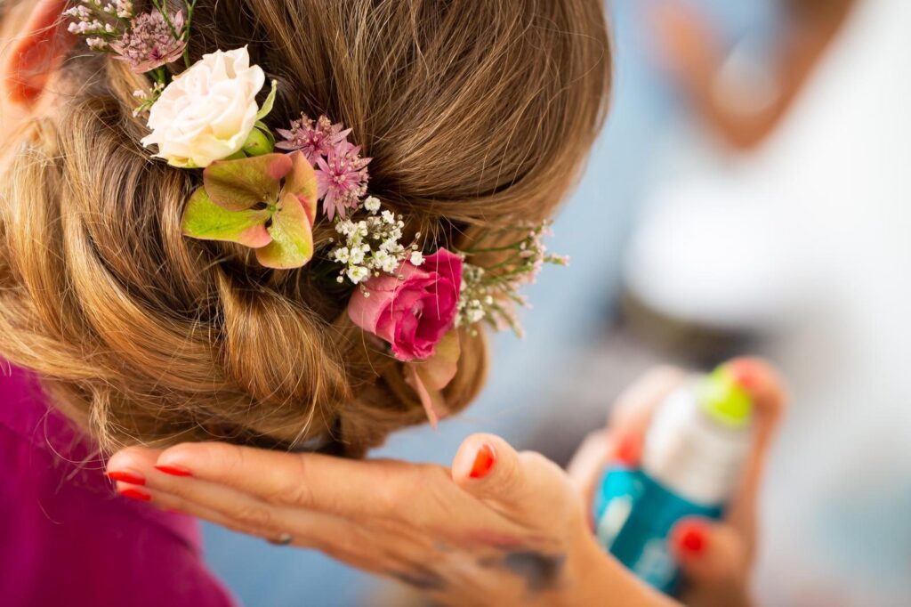 Hochsteckfrisur mit frischen Rosen und Schleierkraut wird zum Schluss mit Haarspray fixiert