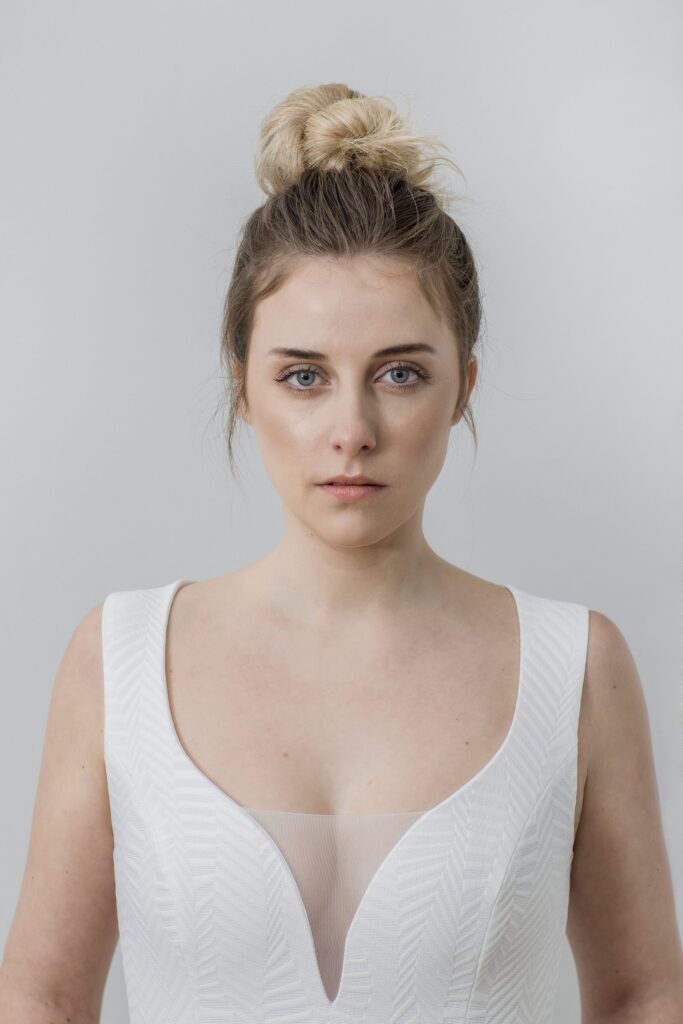 Braut mit hohem, locker gedrehtem Dutt und natürlichem Make-up im Brautkleid mit V-Ausschnitt