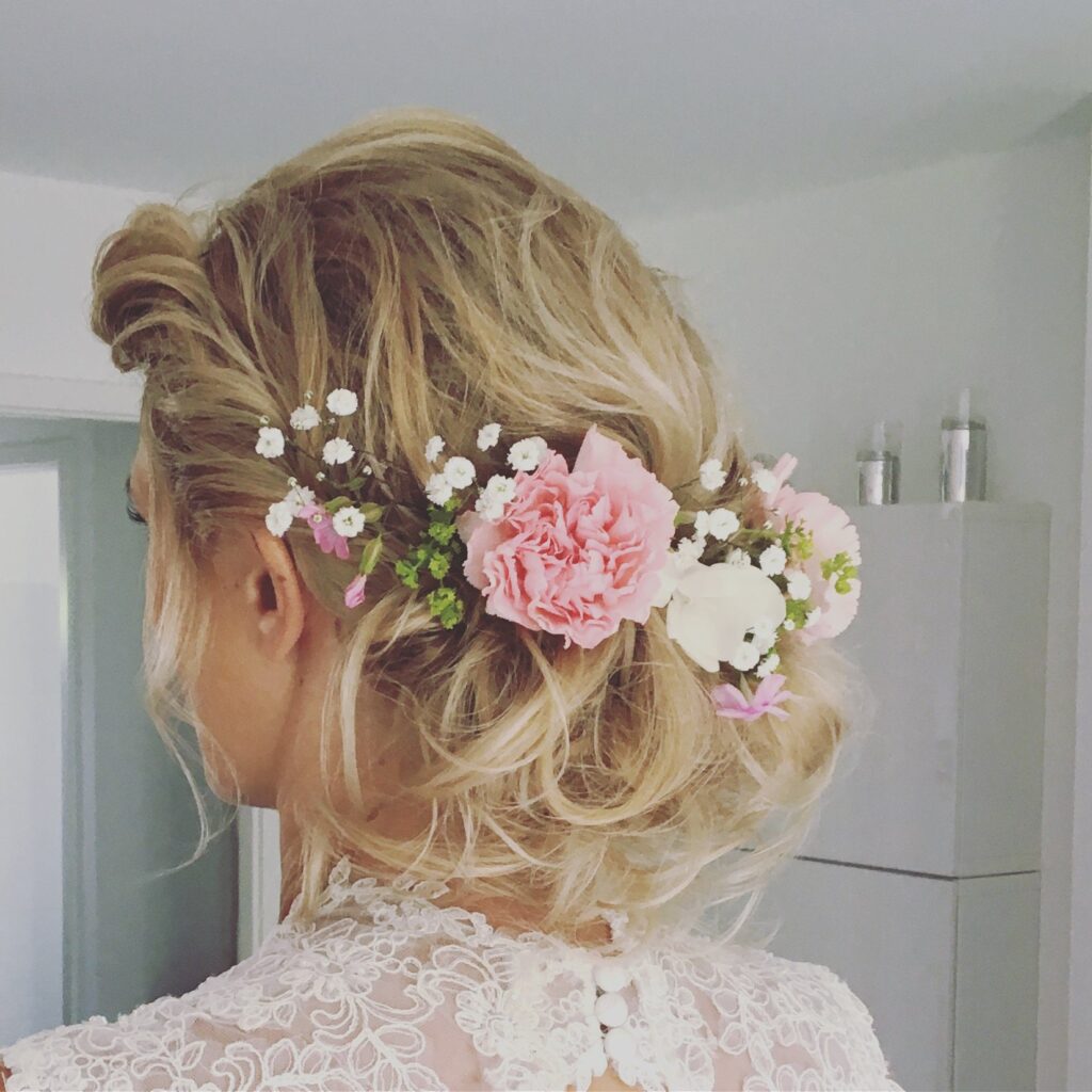 Lockere blonde Hochsteckfrisur mit rosa Nelken und Schleierkraut, Braut im Spitzenkleid